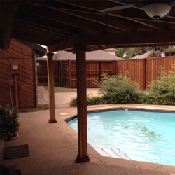 A concrete patio with a patio cover near a pool.